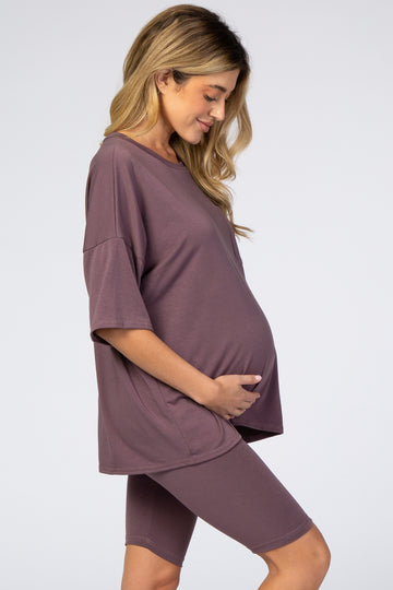 woman wearing a mauve oversized maternity tee and matching bike shorts, cradling her baby bump