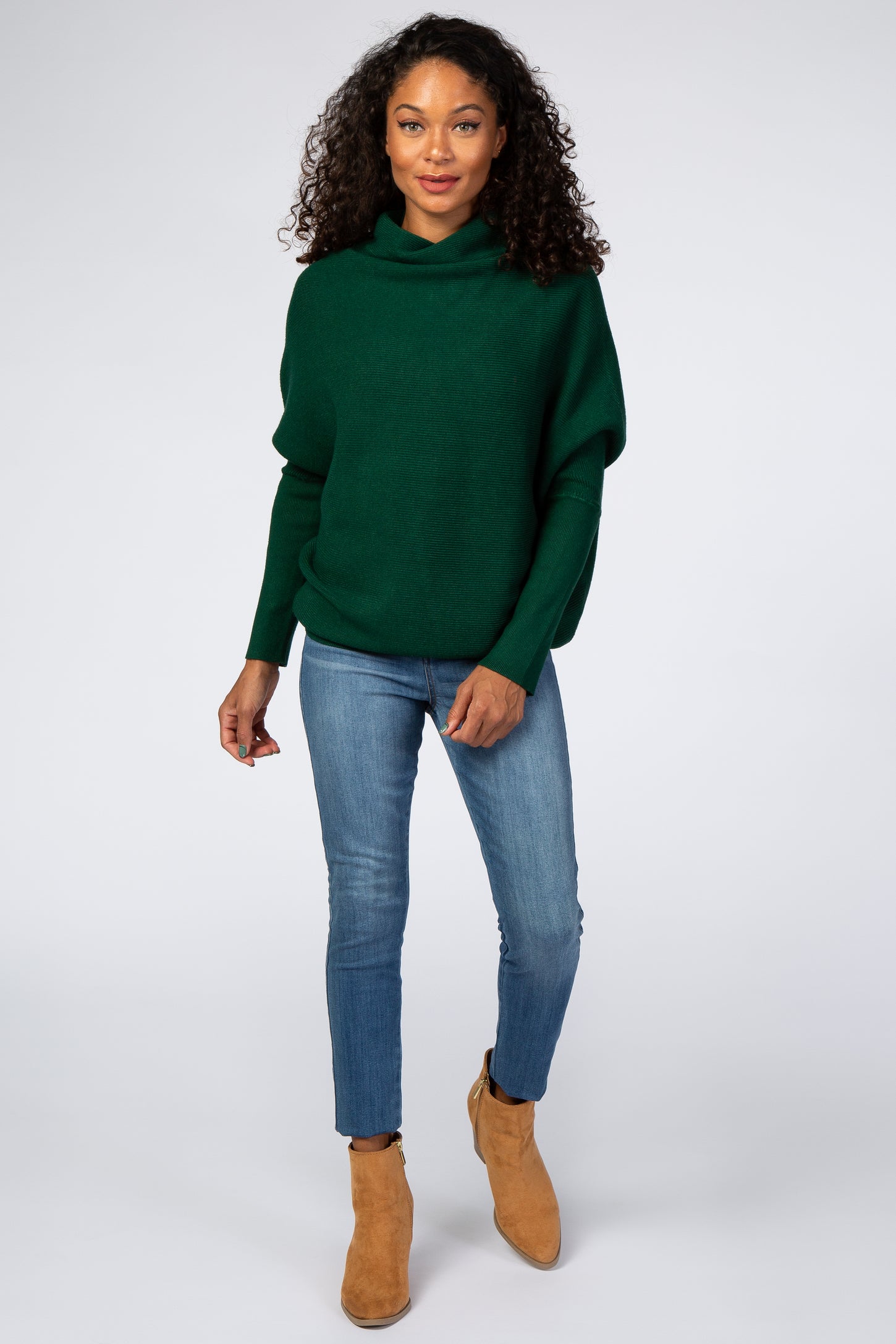 woman wearing a dark green oversized sweater with a hood and blue skinny jeans, paired with tan ankle boots