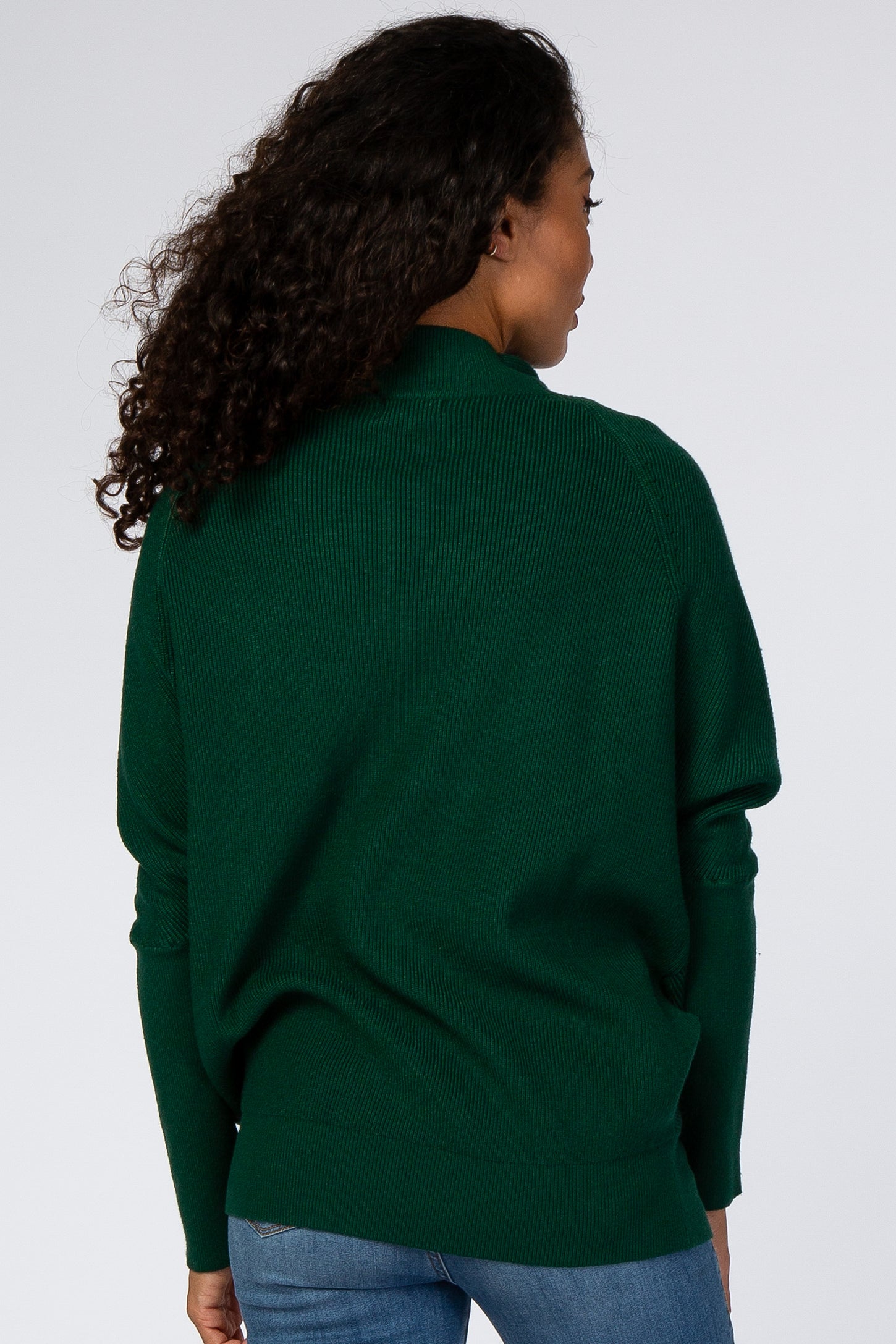 woman wearing a dark green oversized sweater with ribbed texture and long sleeves, shown from the back