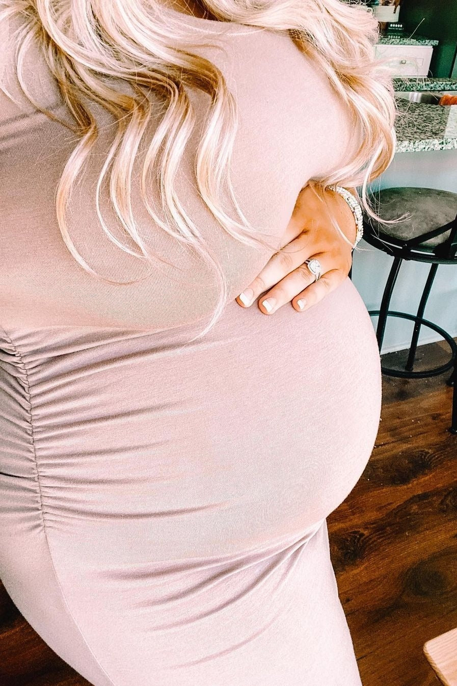 woman wearing a blush pink fitted maternity dress, showcasing her baby bump with side ruching details