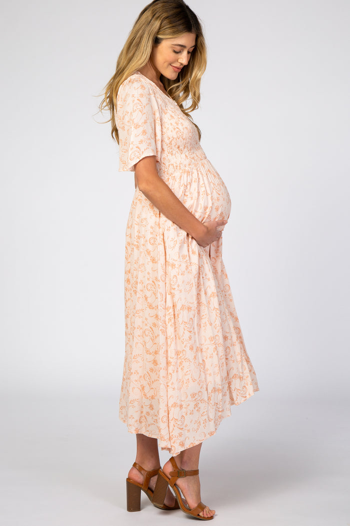 woman wearing a peach floral maternity dress with short sleeves and a baby bump, standing sideways