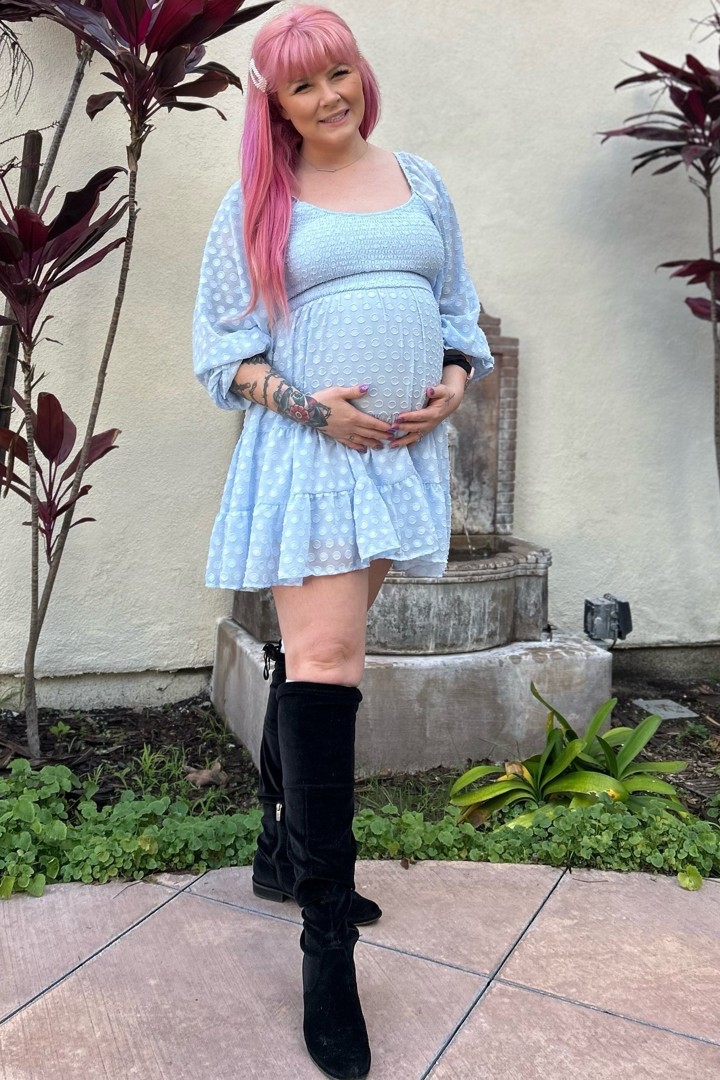 woman wearing a light blue maternity dress with puffed sleeves and holding her baby bump