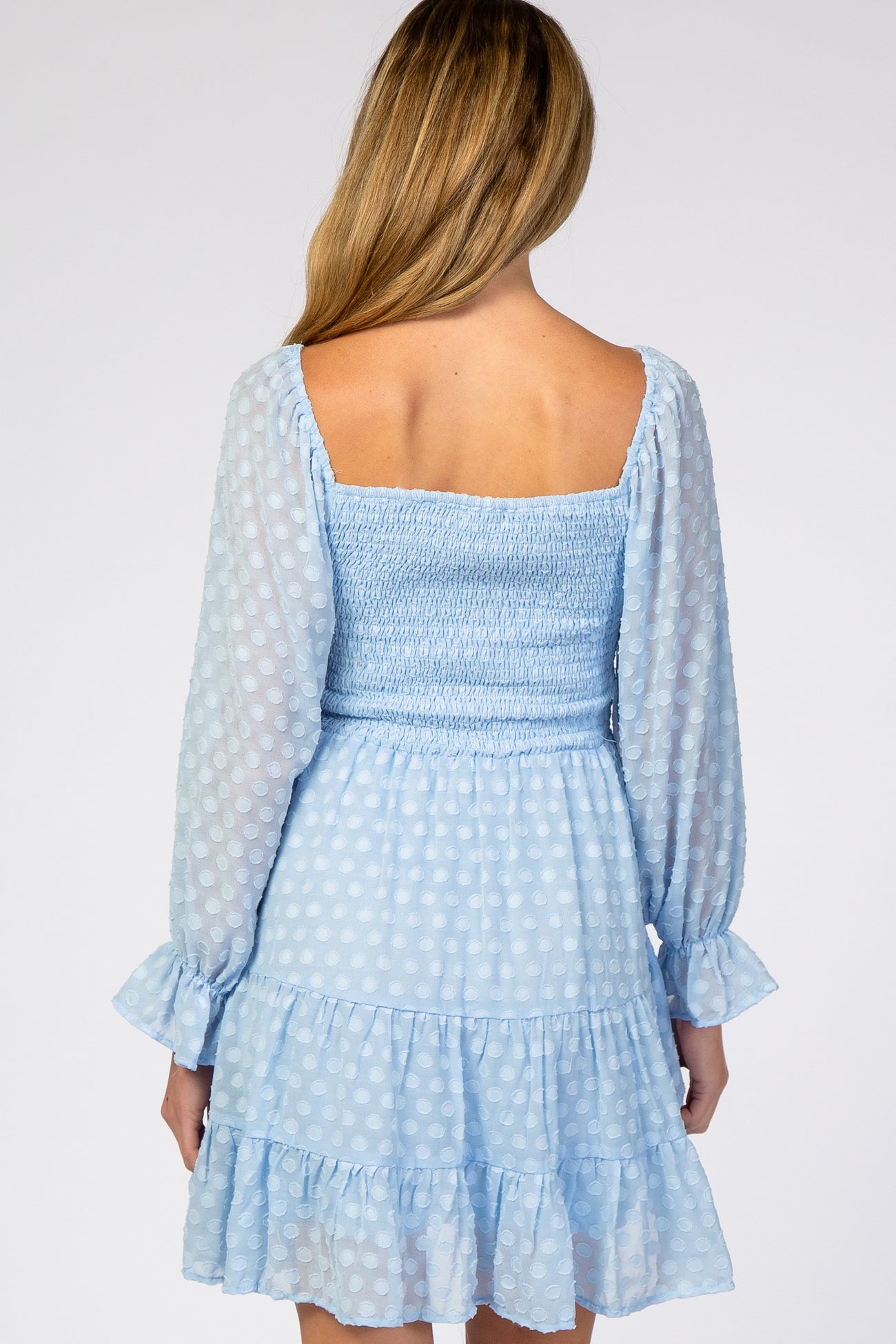 woman wearing a light blue polka dot maternity dress with a smocked bodice and ruffled hem, viewed from the back