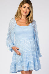 woman wearing a light blue polka dot maternity dress with smocked bodice and tiered ruffle skirt, holding her baby bump