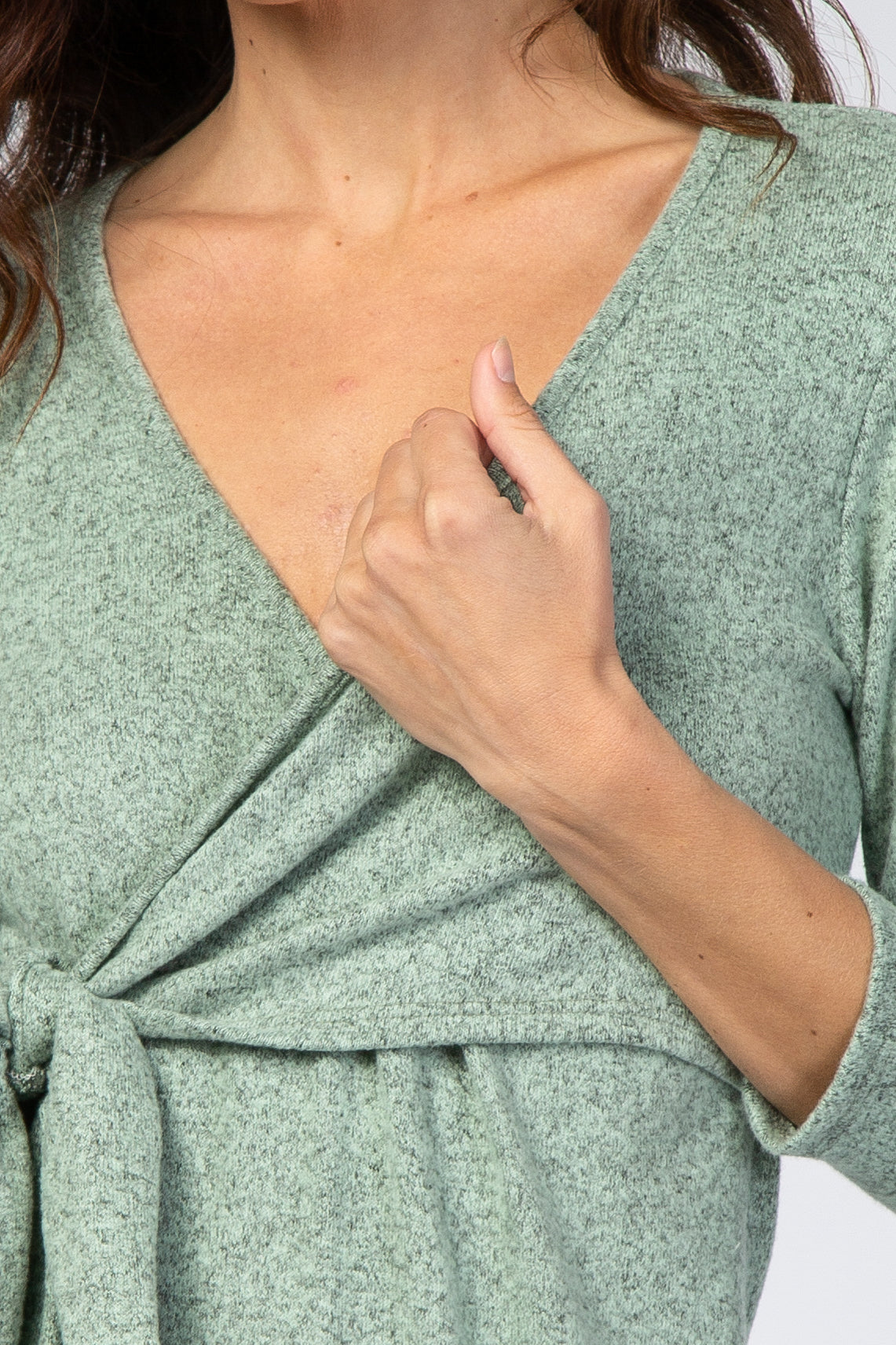 woman wearing a green wrap-style top with a tie detail at the waist and a v-neckline