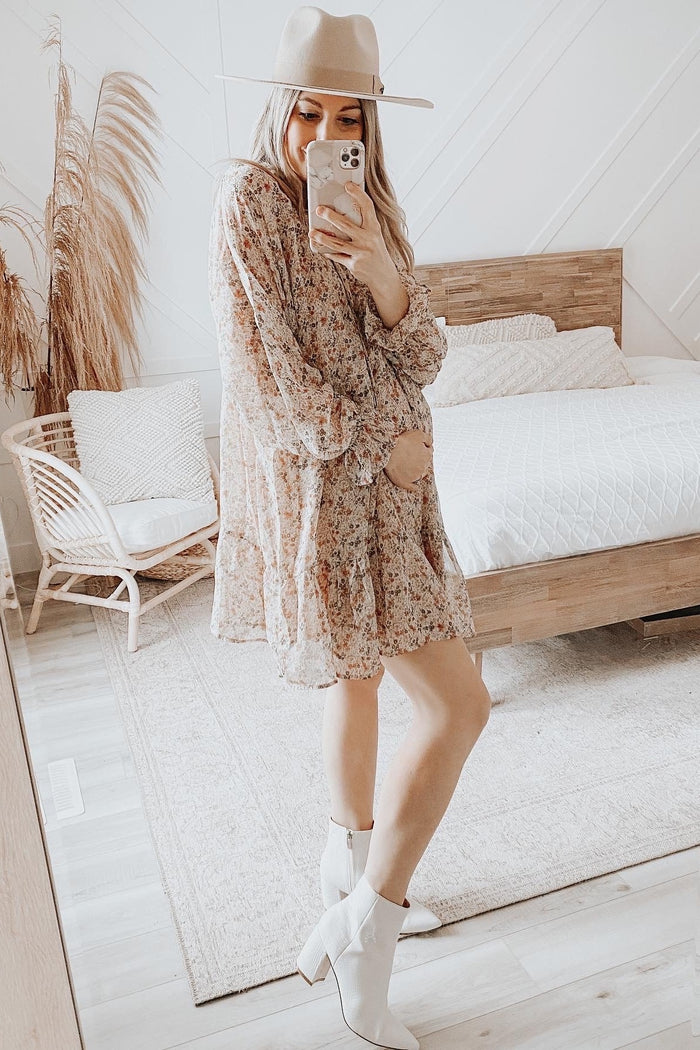 woman wearing a floral maternity dress and showing her baby bump while posing in a stylish room