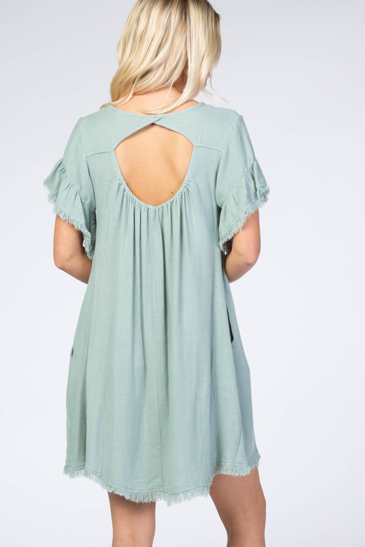 woman wearing a mint green short sleeve dress with back cutout and frayed hem details