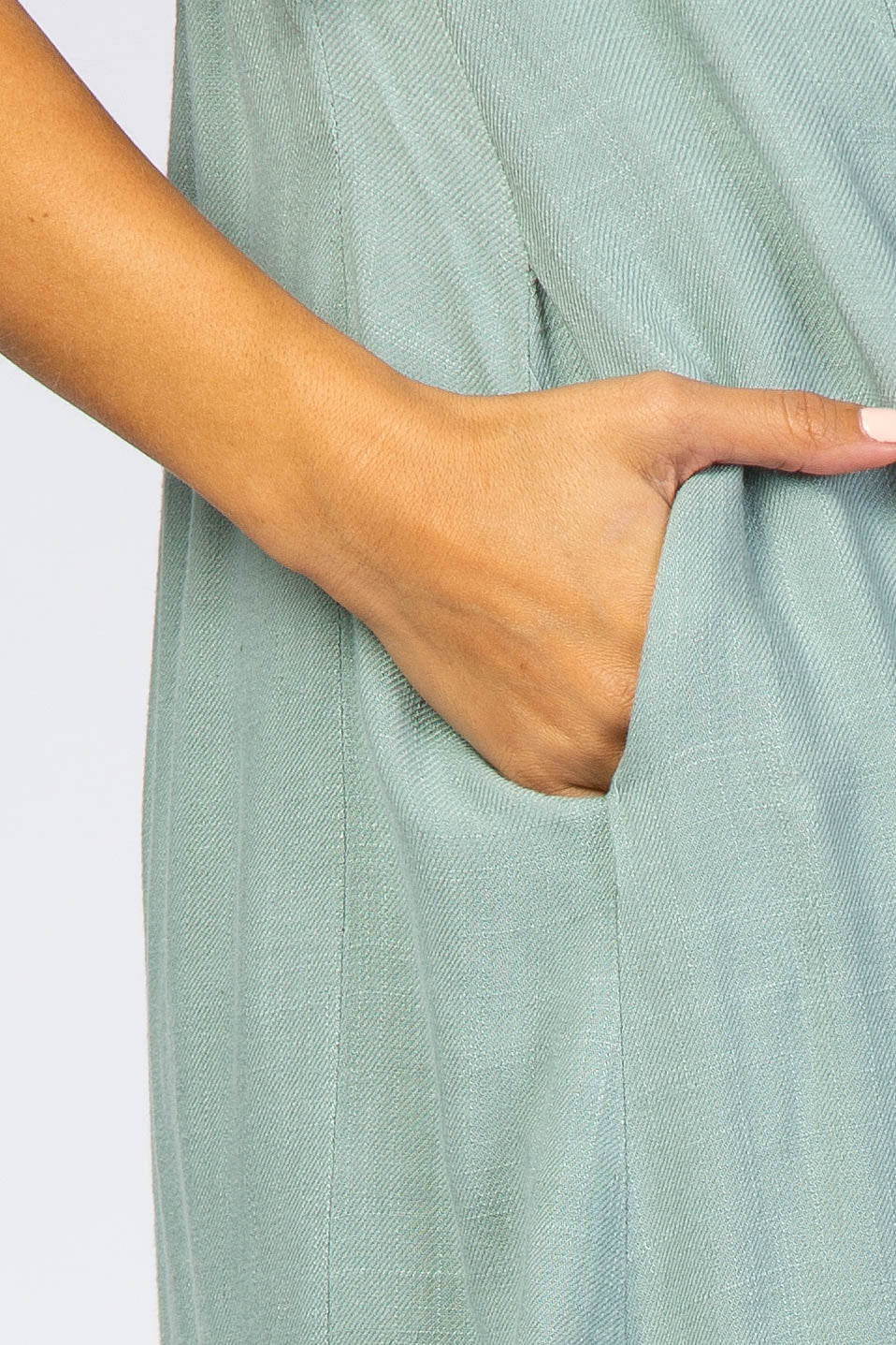 close-up of a woman’s hand reaching into the pocket of a light green maternity dress