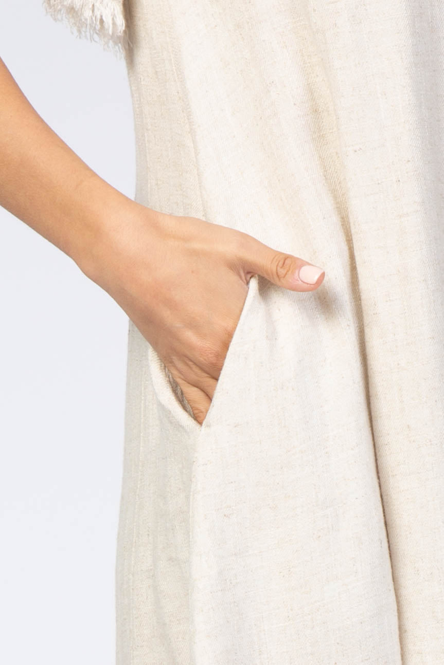 close-up of a woman’s hand reaching into the pocket of a beige linen dress