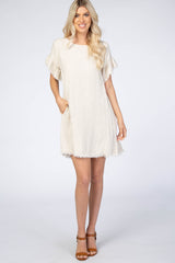 woman wearing a beige short sleeve dress with fringe details and side pockets, standing against a plain background