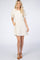 woman wearing a beige short sleeve dress with fringe details and side pockets, standing against a plain background