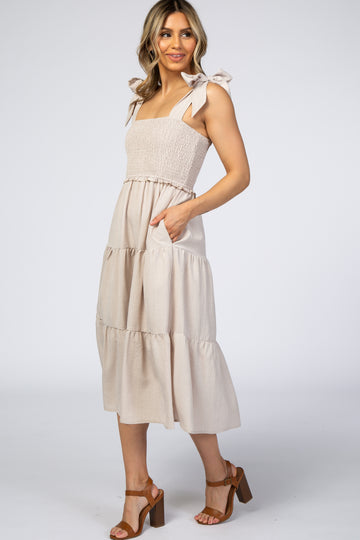 woman wearing a beige smocked maternity midi dress with tie straps and pockets
