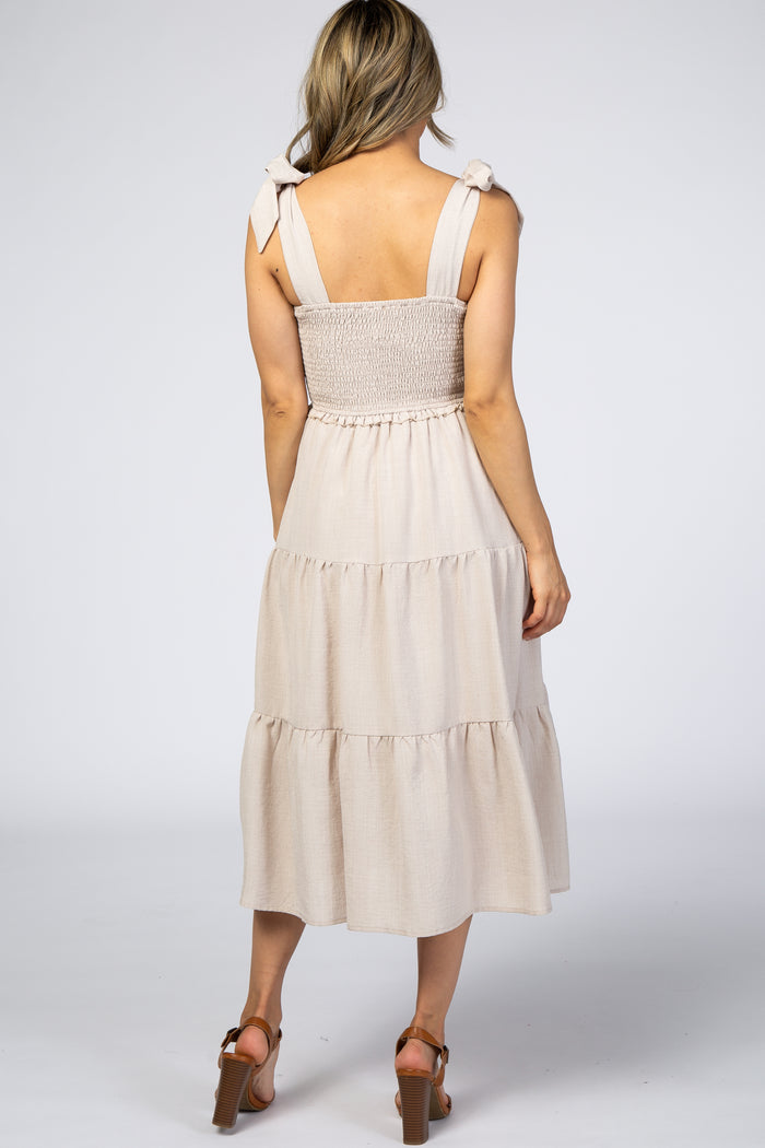 woman wearing a light beige tiered dress with adjustable bow straps and smocked bodice, view from the back