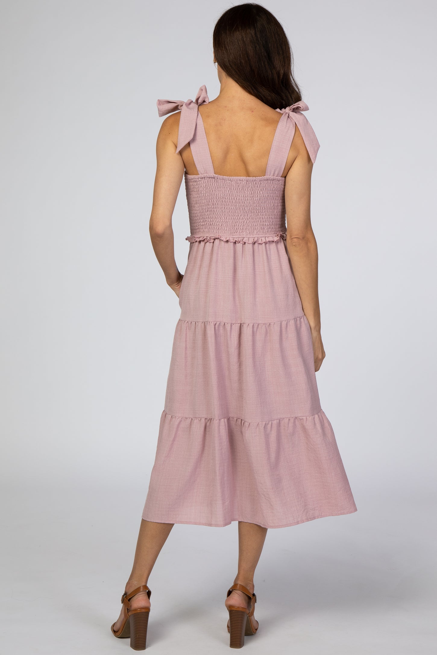 Back view of a woman wearing a mauve tiered midi dress with tie straps and a smocked bodice