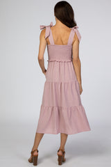 Back view of a woman wearing a mauve tiered midi dress with tie straps and a smocked bodice