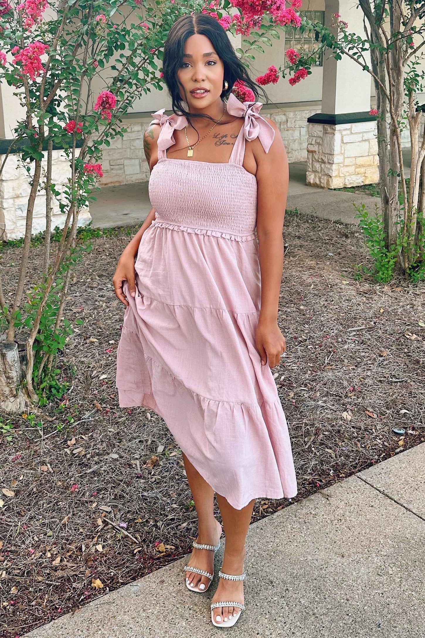 woman wearing a pink smocked sundress with tie straps and a tiered skirt, standing in a garden setting