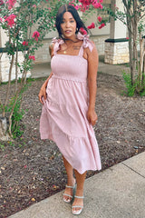 woman wearing a pink smocked sundress with tie straps and a tiered skirt, standing in a garden setting