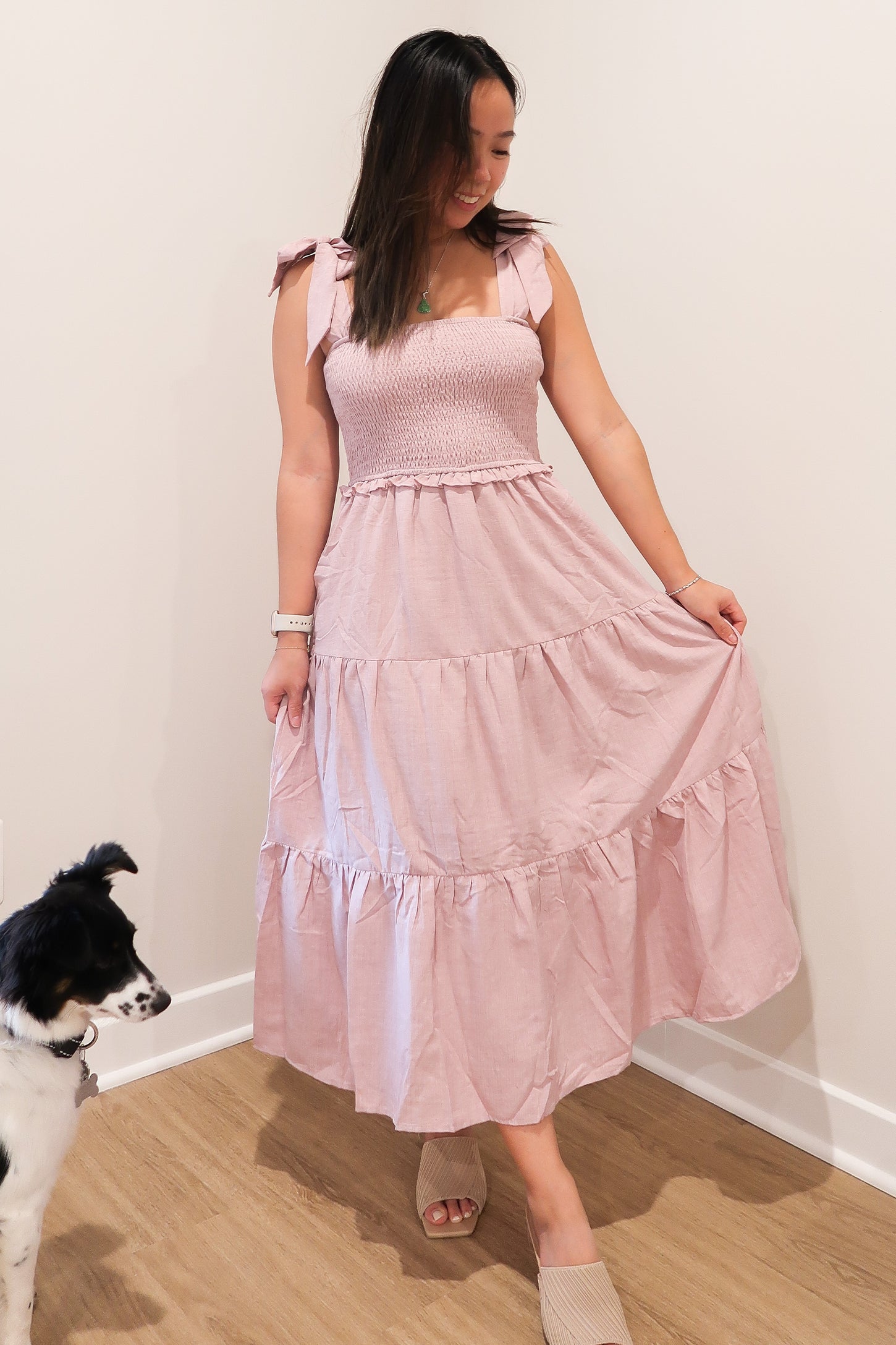 woman wearing a pink smocked maxi dress with ruffled straps and a tiered skirt, standing next to a dog
