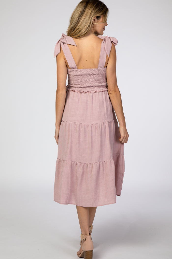 woman wearing a pink smocked maternity dress with tie straps and a tiered skirt, visible baby bump