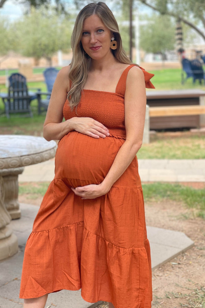 woman wearing an orange maternity dress with smocked bodice and tiered skirt, holding her baby bump