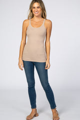 woman wearing a beige ribbed tank top and blue skinny jeans, standing and smiling at the camera