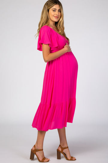 woman wearing a bright pink maternity dress with flutter sleeves and a tiered hem, cradling her baby bump