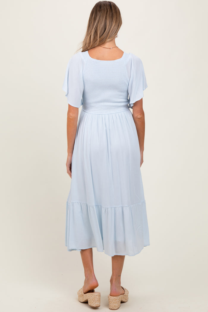 woman wearing a light blue maternity dress with a smocked bodice and tiered skirt, showing the back view