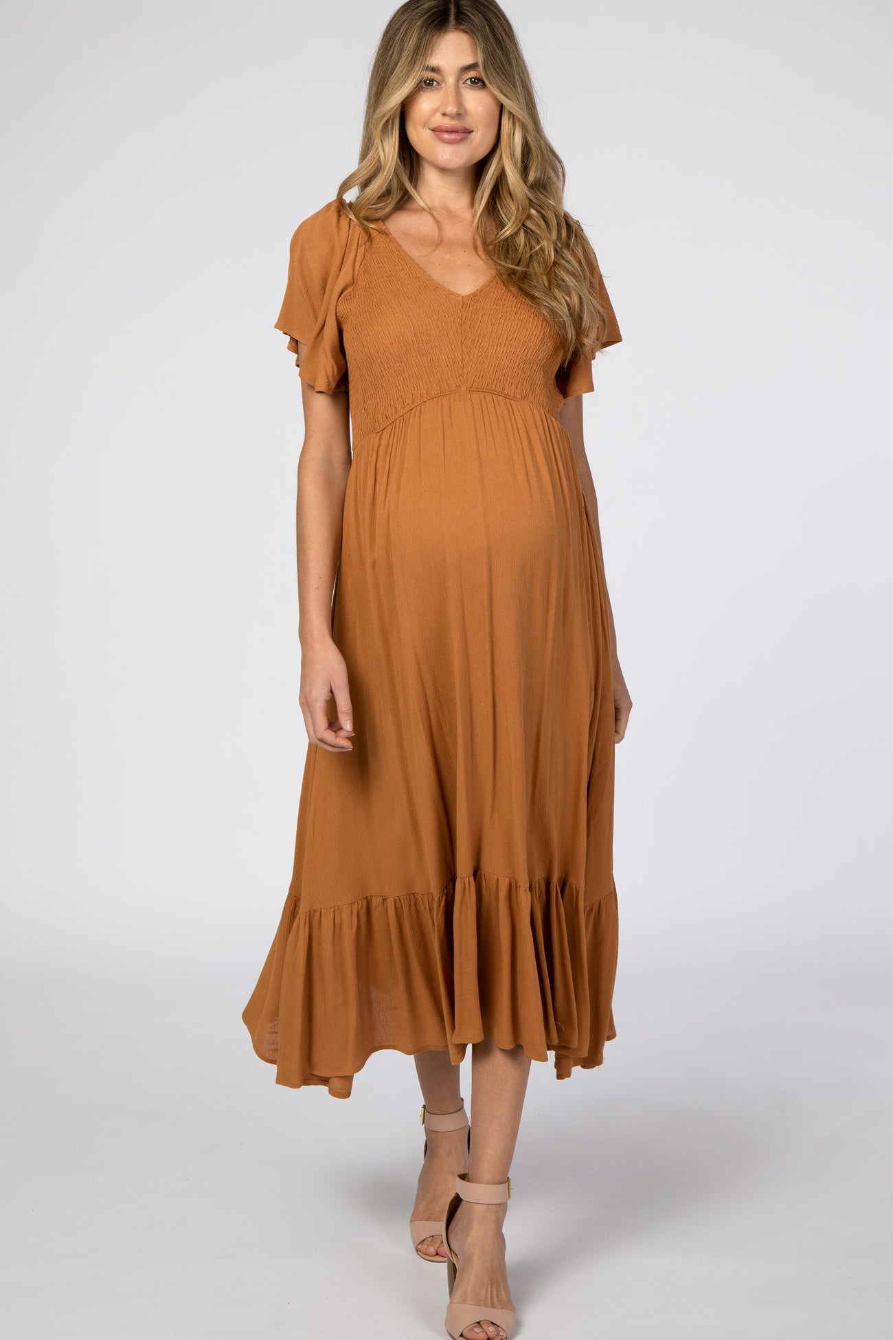 woman wearing a rust-colored maternity dress with flutter sleeves and a ruffled hem, showcasing her baby bump