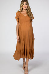 woman wearing a rust-colored maternity dress with flutter sleeves and a ruffled hem, showcasing her baby bump