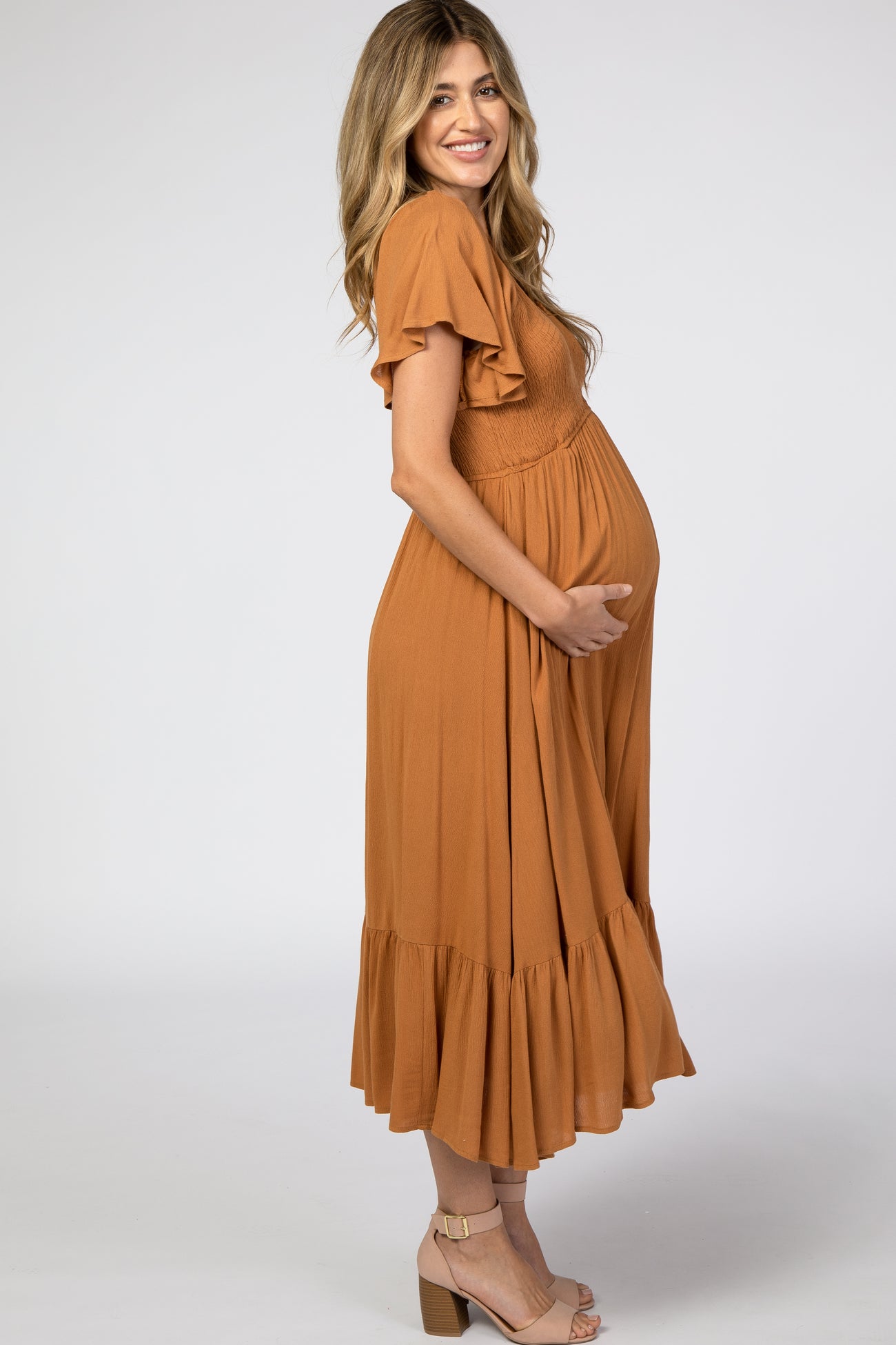 woman wearing an orange maternity dress with ruffled sleeves and a tiered skirt, gently cradling her baby bump