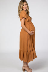woman wearing an orange maternity dress with ruffled sleeves and a tiered skirt, gently cradling her baby bump