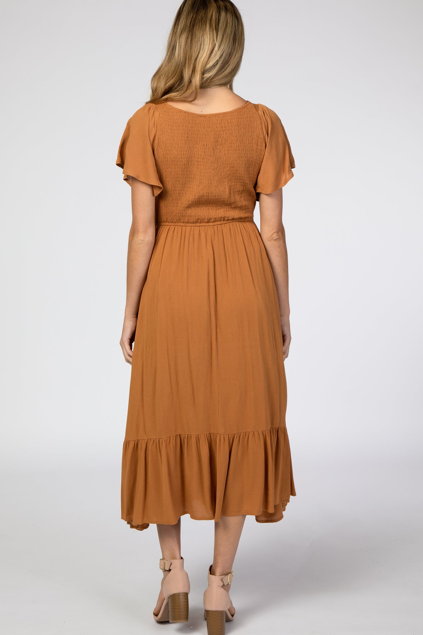 Back view of a woman wearing a rust orange smocked midi dress with flutter sleeves and tan block heels