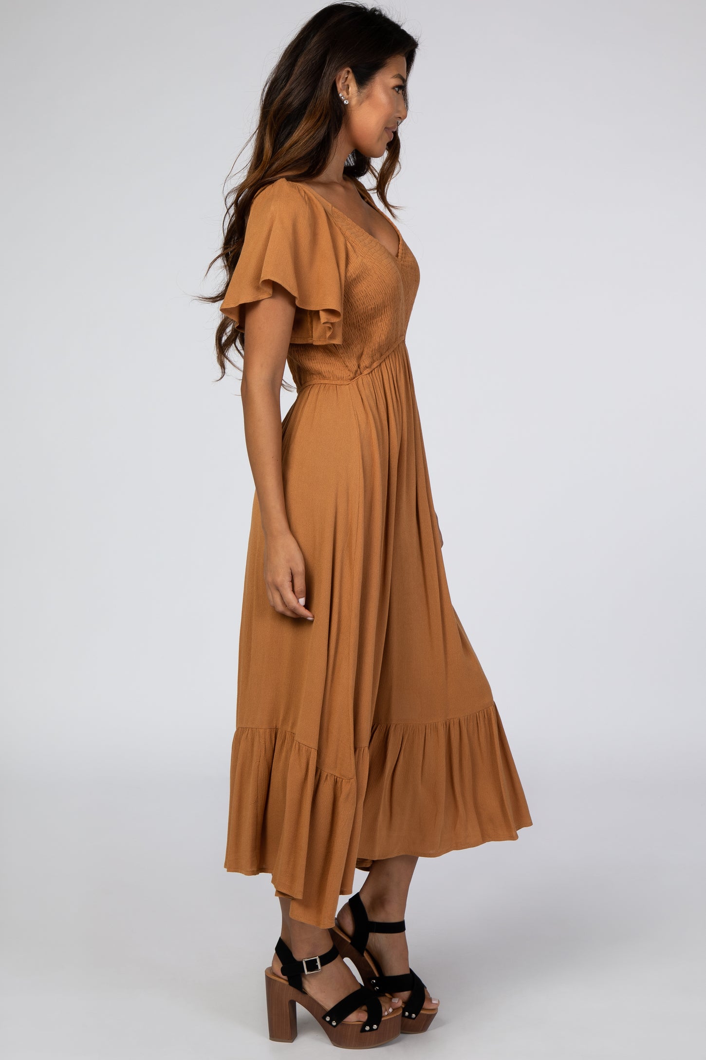 woman wearing a rust colored midi dress with short flutter sleeves and a tiered skirt, paired with black block heel sandals