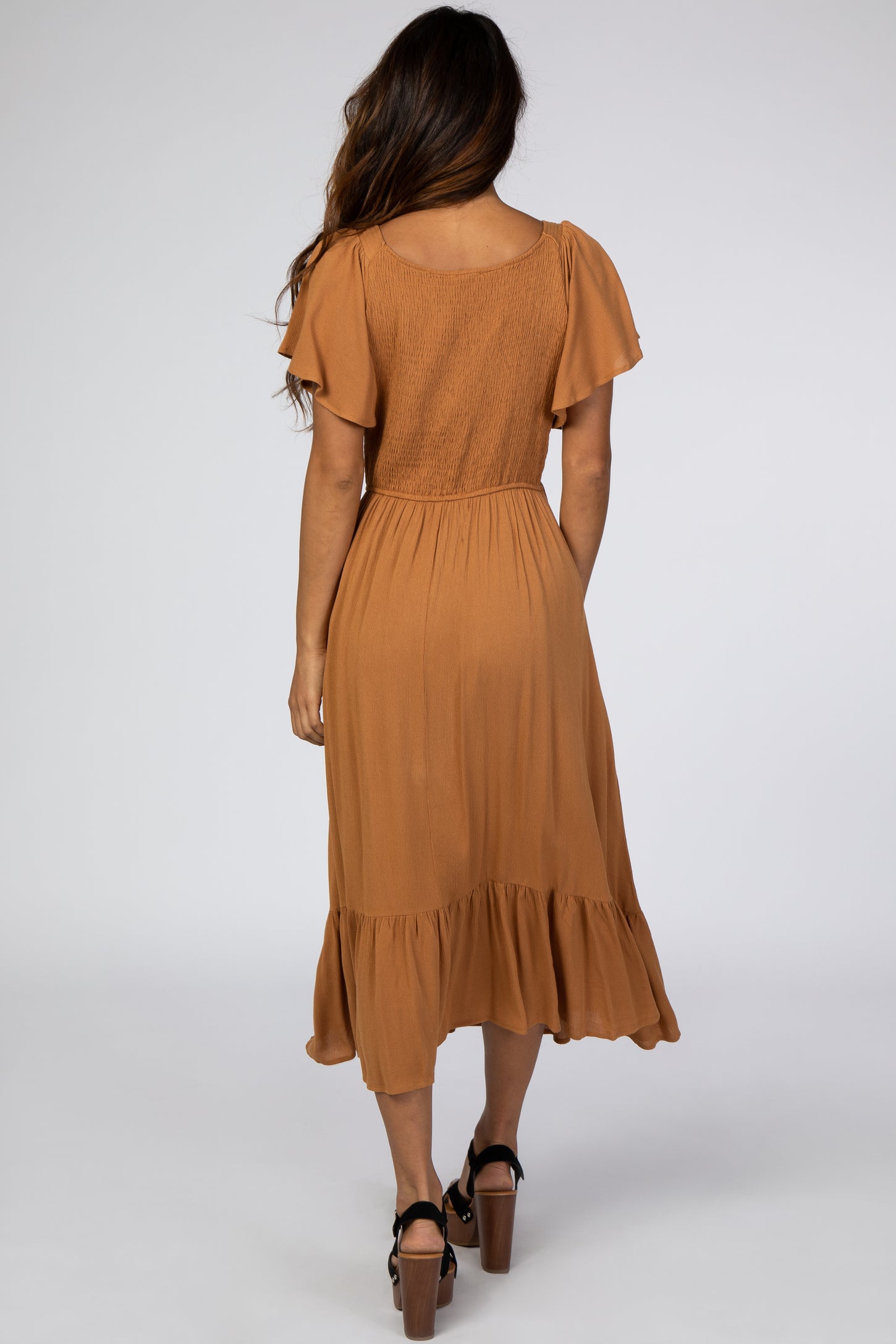 woman wearing a rust-colored midi dress with flutter sleeves and a ruffled hem, viewed from the back