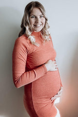 woman wearing an orange long sleeve fitted maternity dress and holding her baby bump
