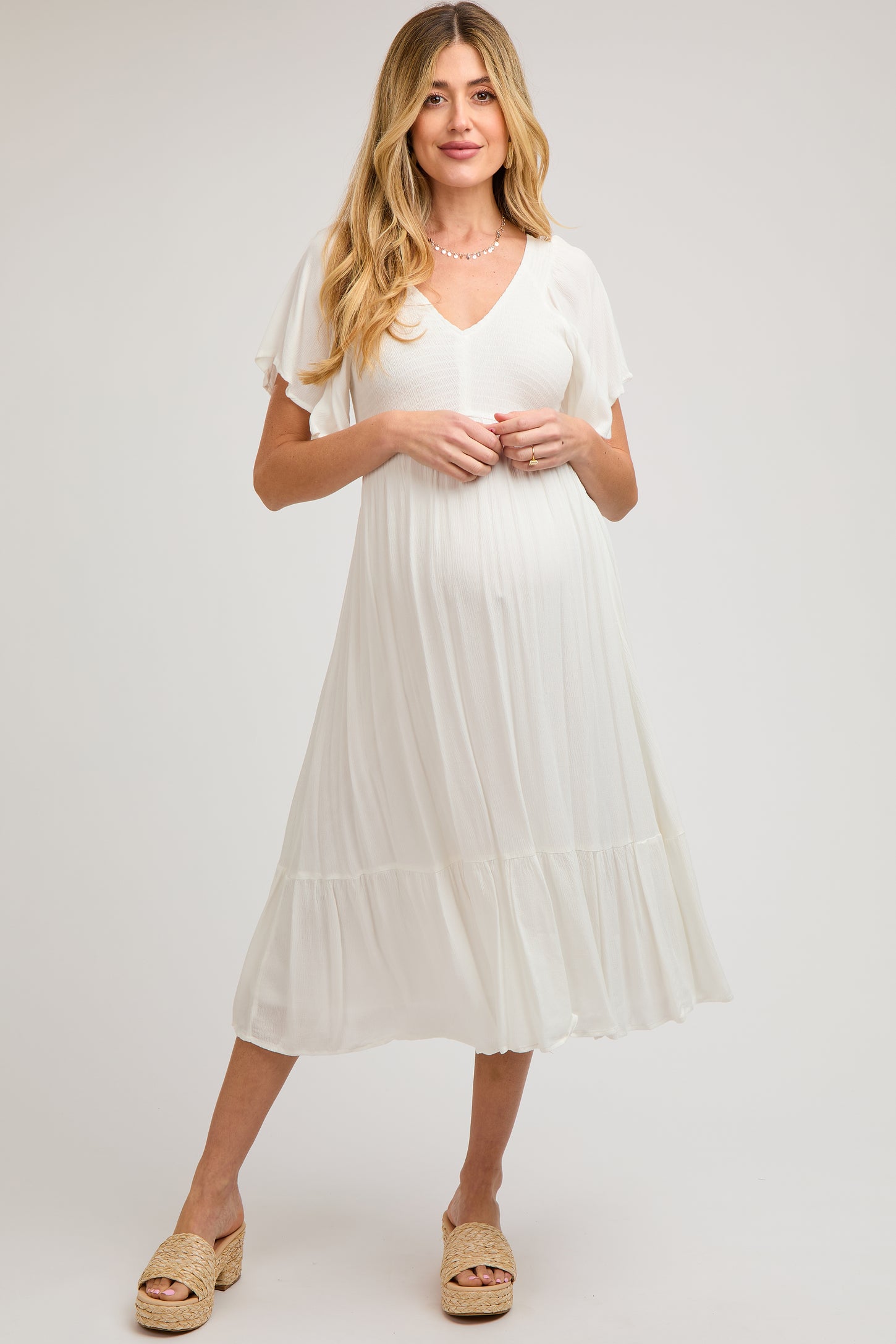 woman wearing a white maternity dress with flutter sleeves and a tiered hem, showcasing her baby bump