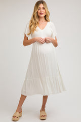 woman wearing a white maternity dress with flutter sleeves and a tiered hem, showcasing her baby bump