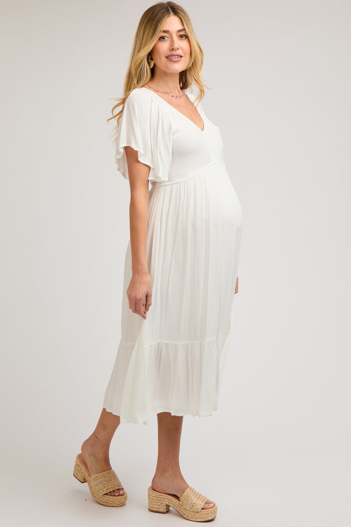 woman wearing a white maternity dress with flutter sleeves and a flowing skirt, highlighting her baby bump