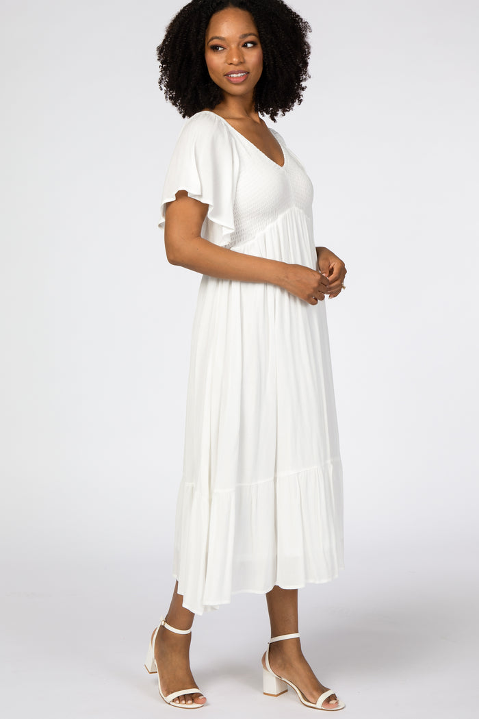 woman wearing a white midi dress with short flutter sleeves and a tiered hem, standing in profile