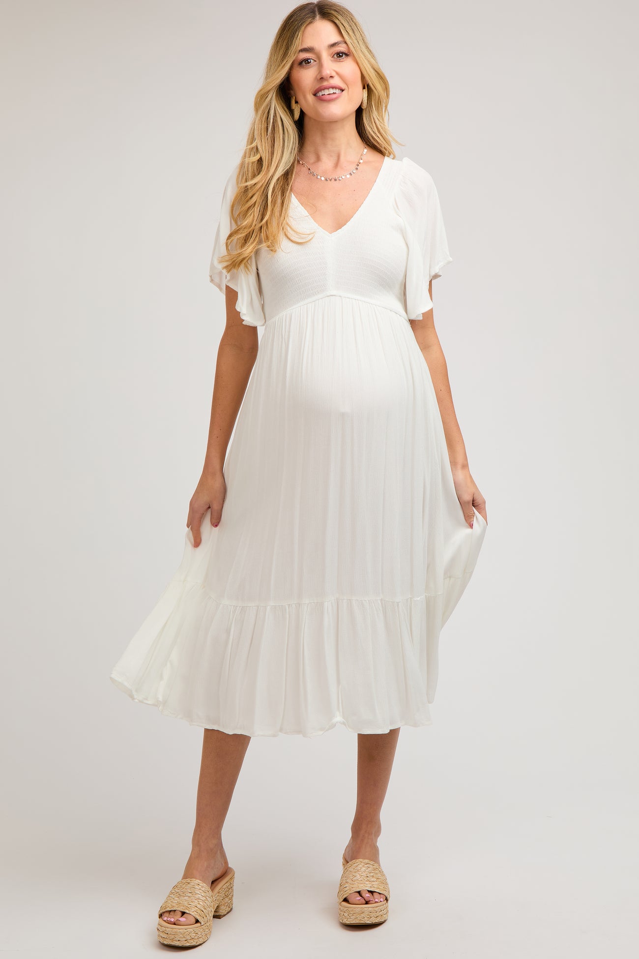 woman wearing a white maternity dress with a v-neck and flutter sleeves, holding her baby bump