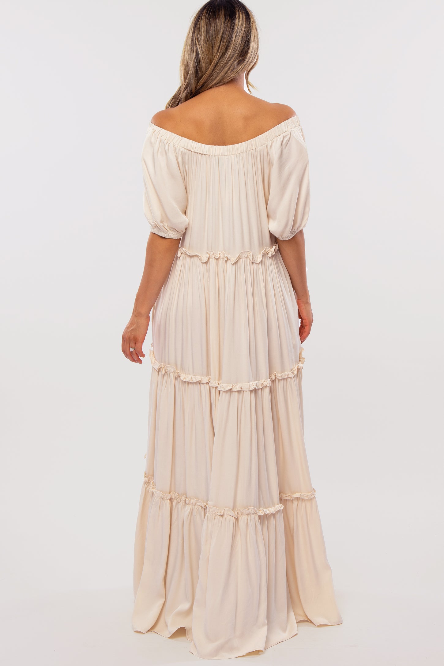 woman wearing a light beige off-the-shoulder maxi dress with puffed sleeves and tiered ruffle details
