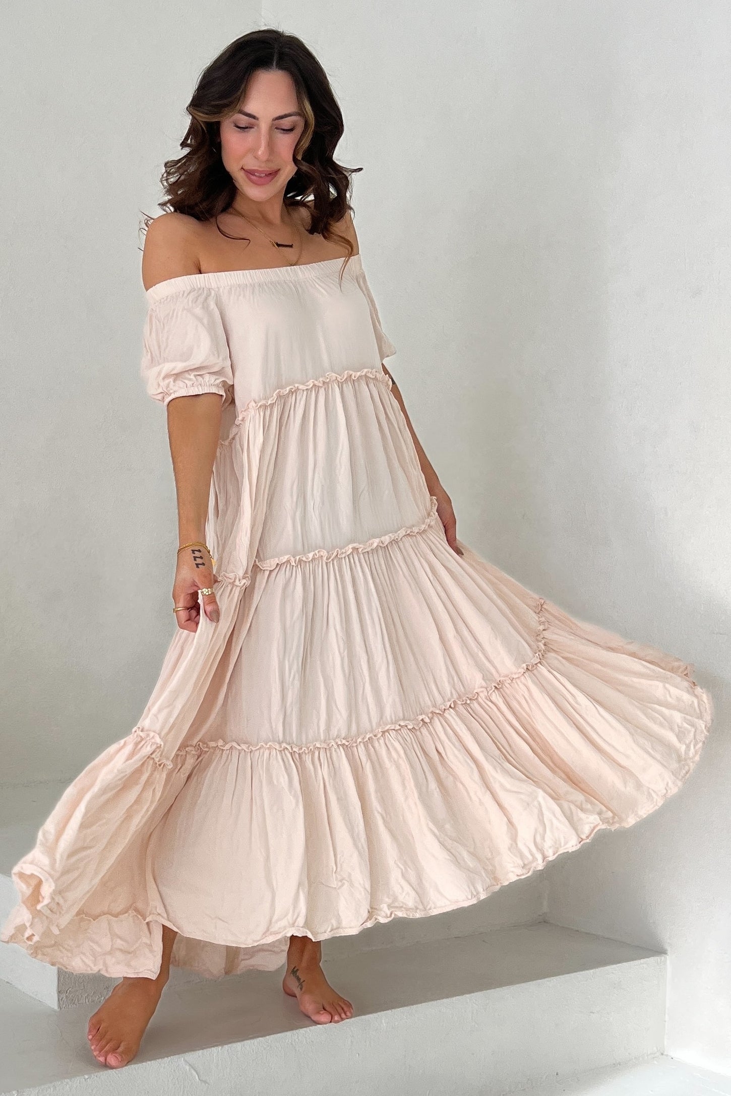 woman wearing a light pink off-the-shoulder maxi dress with tiered ruffles and flowing silhouette