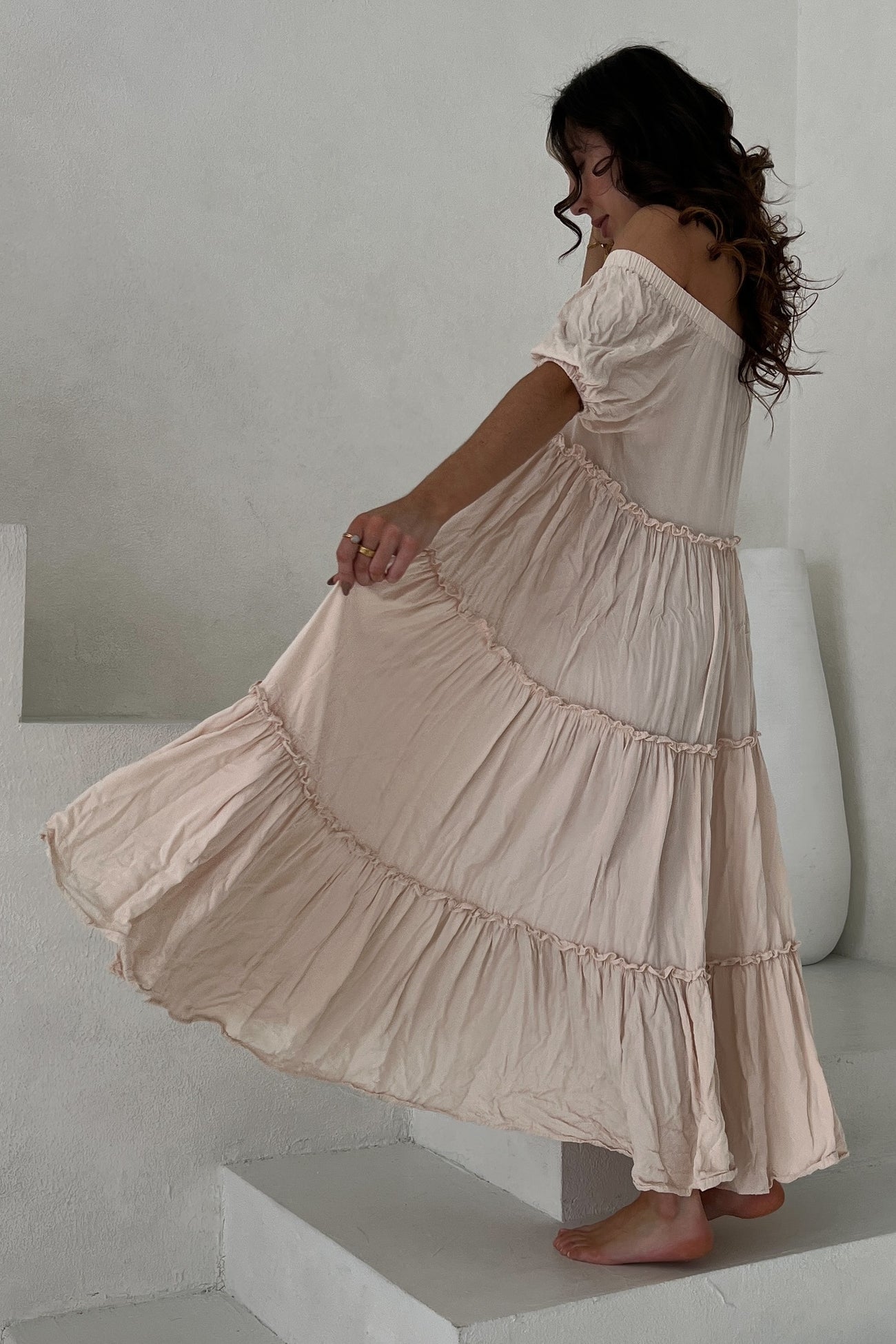 woman wearing a soft pink off-the-shoulder maxi dress with tiered ruffles, twirling on stairs