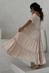 woman wearing a soft pink off-the-shoulder maxi dress with tiered ruffles, twirling on stairs
