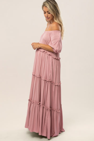 woman wearing a pink off-the-shoulder maternity maxi dress with tiered ruffles and a visible baby bump