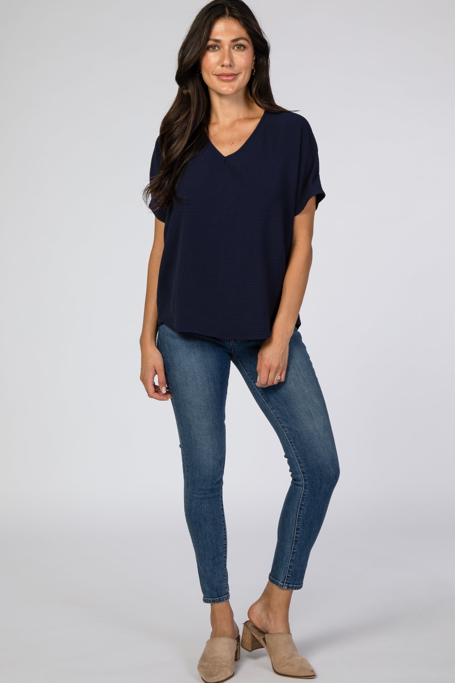 woman wearing a navy blue short sleeve v-neck top with jeans and beige mules