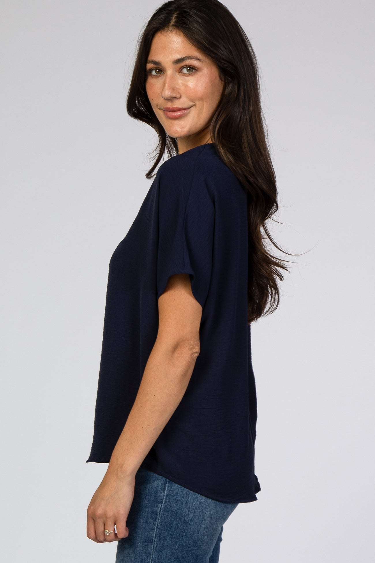 woman wearing a navy blue short sleeve top with a relaxed fit and standing sideways towards the camera