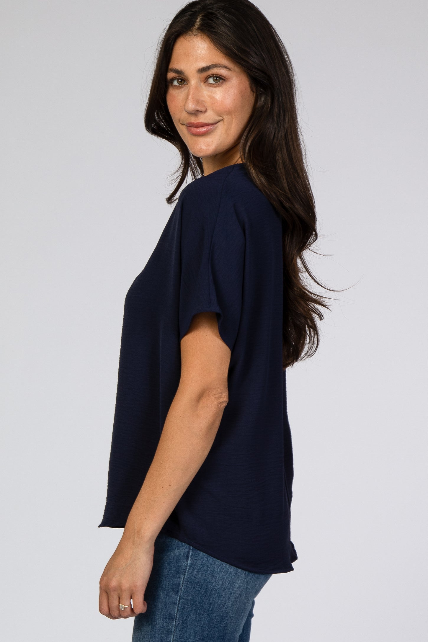 woman wearing a navy blue short sleeve top with a relaxed fit and standing sideways towards the camera