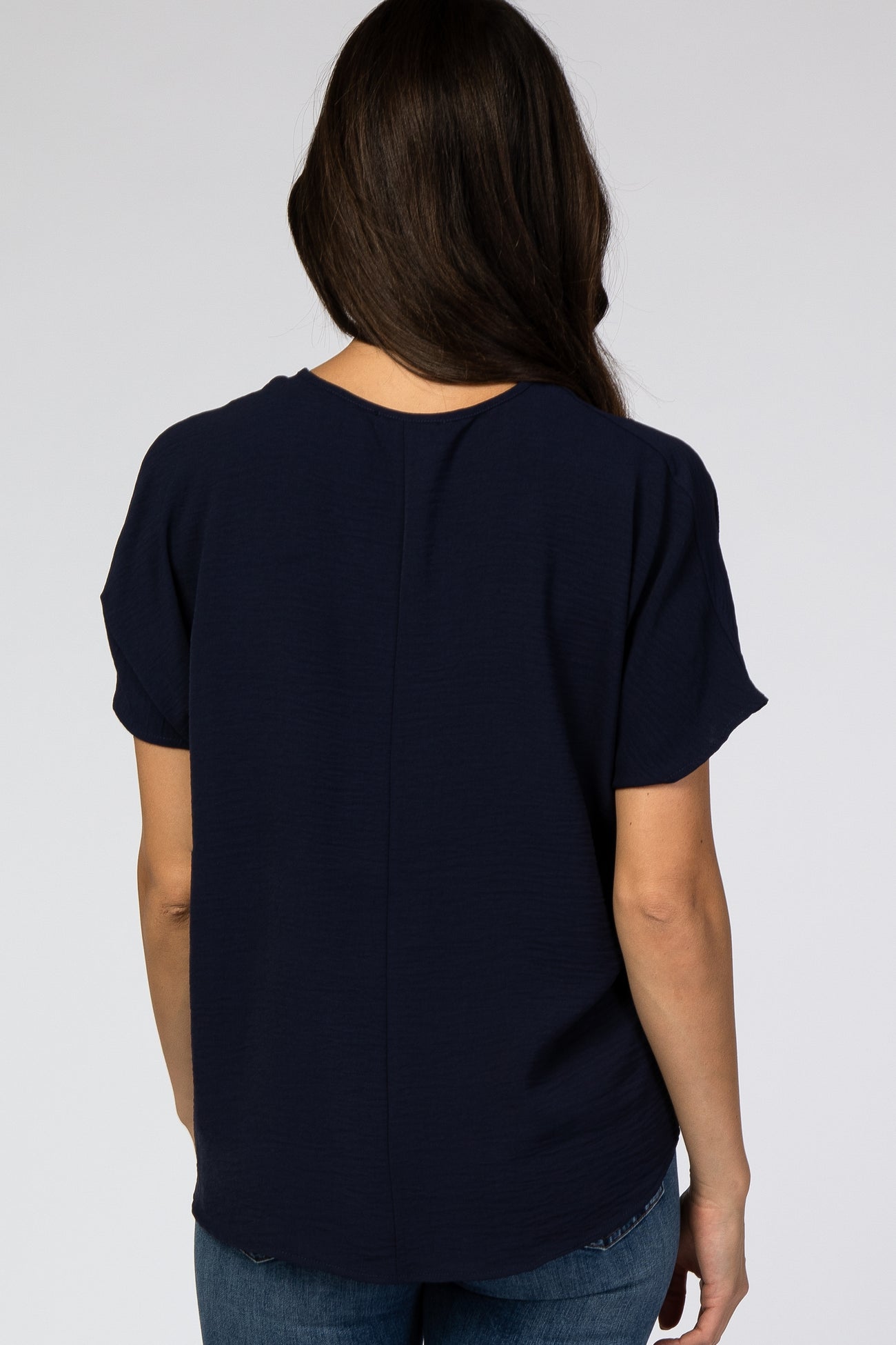 woman wearing a navy blue short sleeve top, seen from the back, with a relaxed fit and rounded hemline