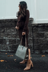 woman wearing a brown maternity dress with a tie waist and a visible baby bump, carrying a gray handbag and wearing ankle boots